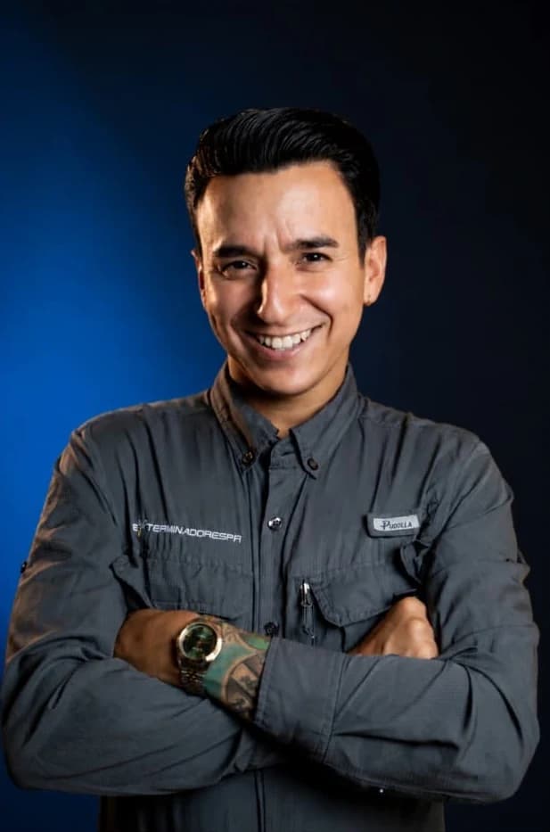 Emanuel Calero, fundador de Exterminadores PR, de brazos cruzados en camisa de uniforme sobre fondo azul de estudio
