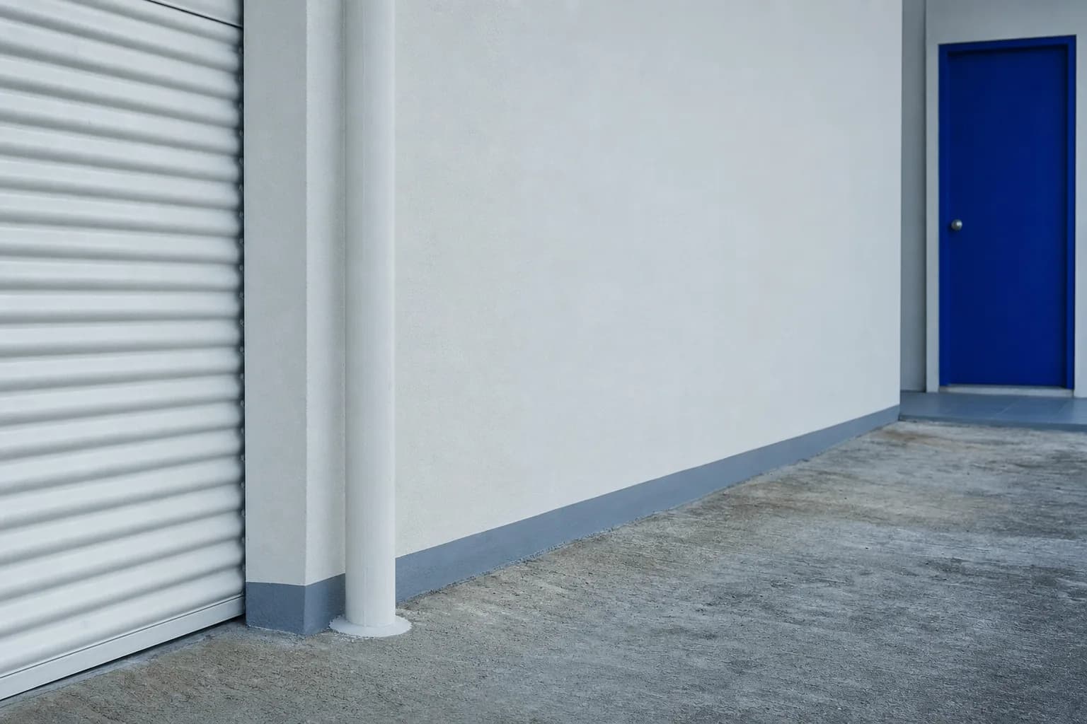 Tubería sellada al muro junto a una puerta de garaje y una puerta azul