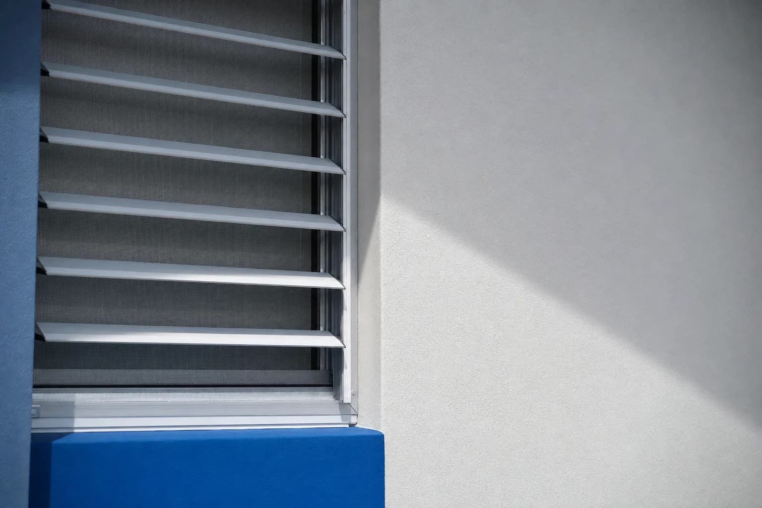 Persiana de aluminio con tela metálica tensa junto a un muro azul